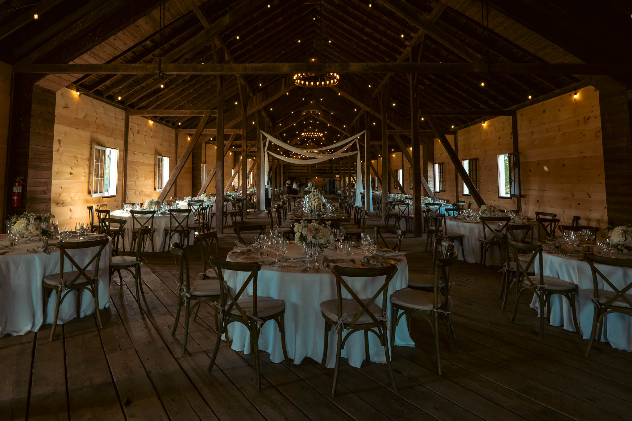 Reception tables set under the string lights in the barn — Sylvanside Farm wedding in Purcellville, Virginia